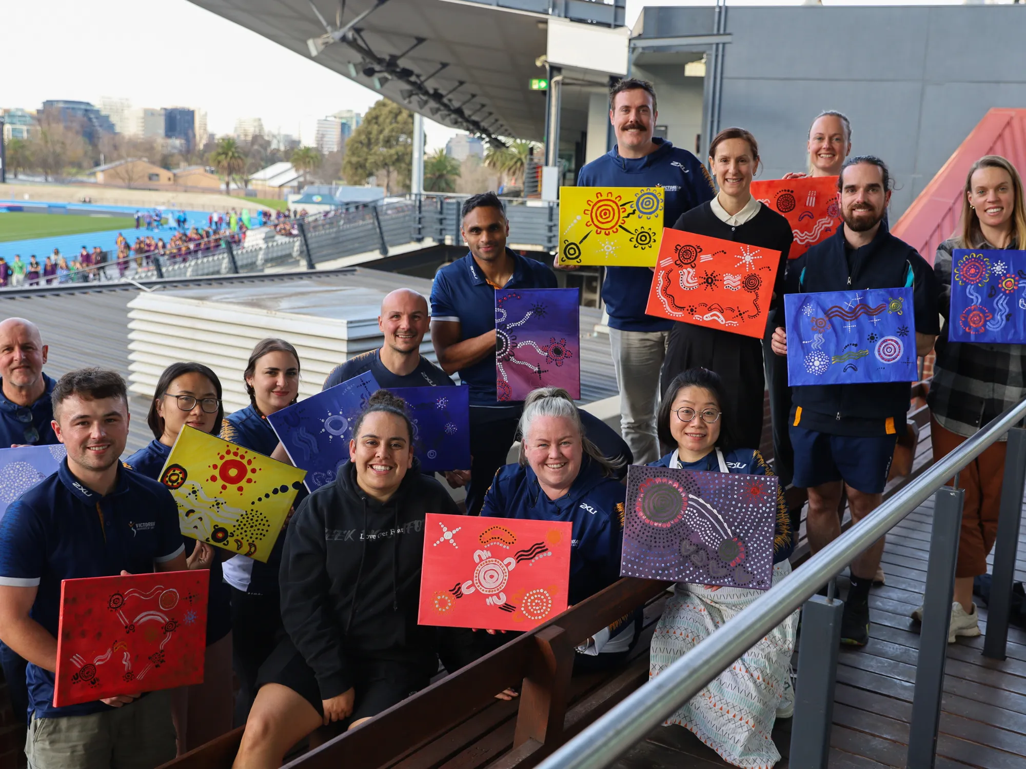 A group photo of over fifteen staff members holding up their painted canvas of first nations artwork.