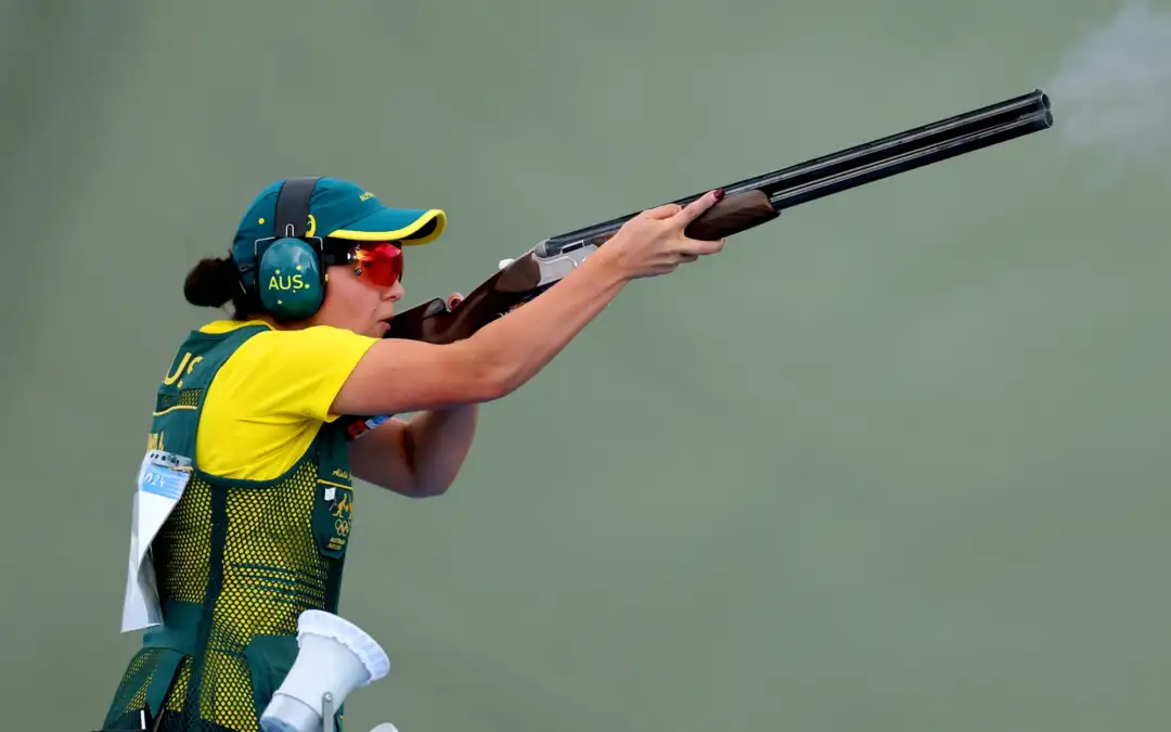 A female wearing Australian Olympic Team uniform holds a rifle for aim.