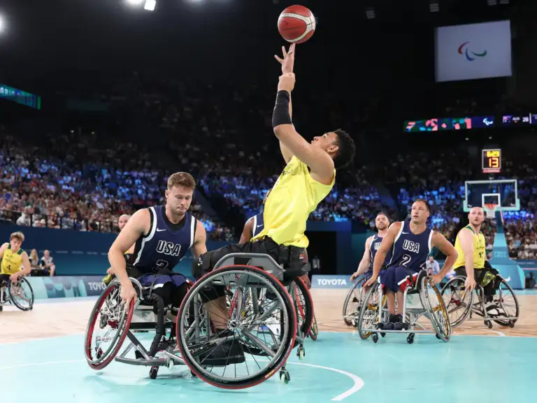 A male athlete in his twenties who is a wheelchair user is performing a basketball layup during a wheelchair basketball match.