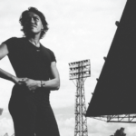 A black and white photo of a women in her thirties wearing a black tee, looking into the distance.