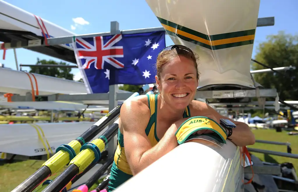 Female Olympian representing Australia leaning over her racing shell for rowing smiling at the camera.