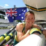 Female Olympian representing Australia leaning over her racing shell for rowing smiling at the camera.