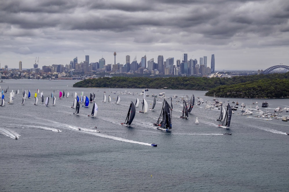 An aerial photo of over 100 sailing boats leaving Sydney's harbor.