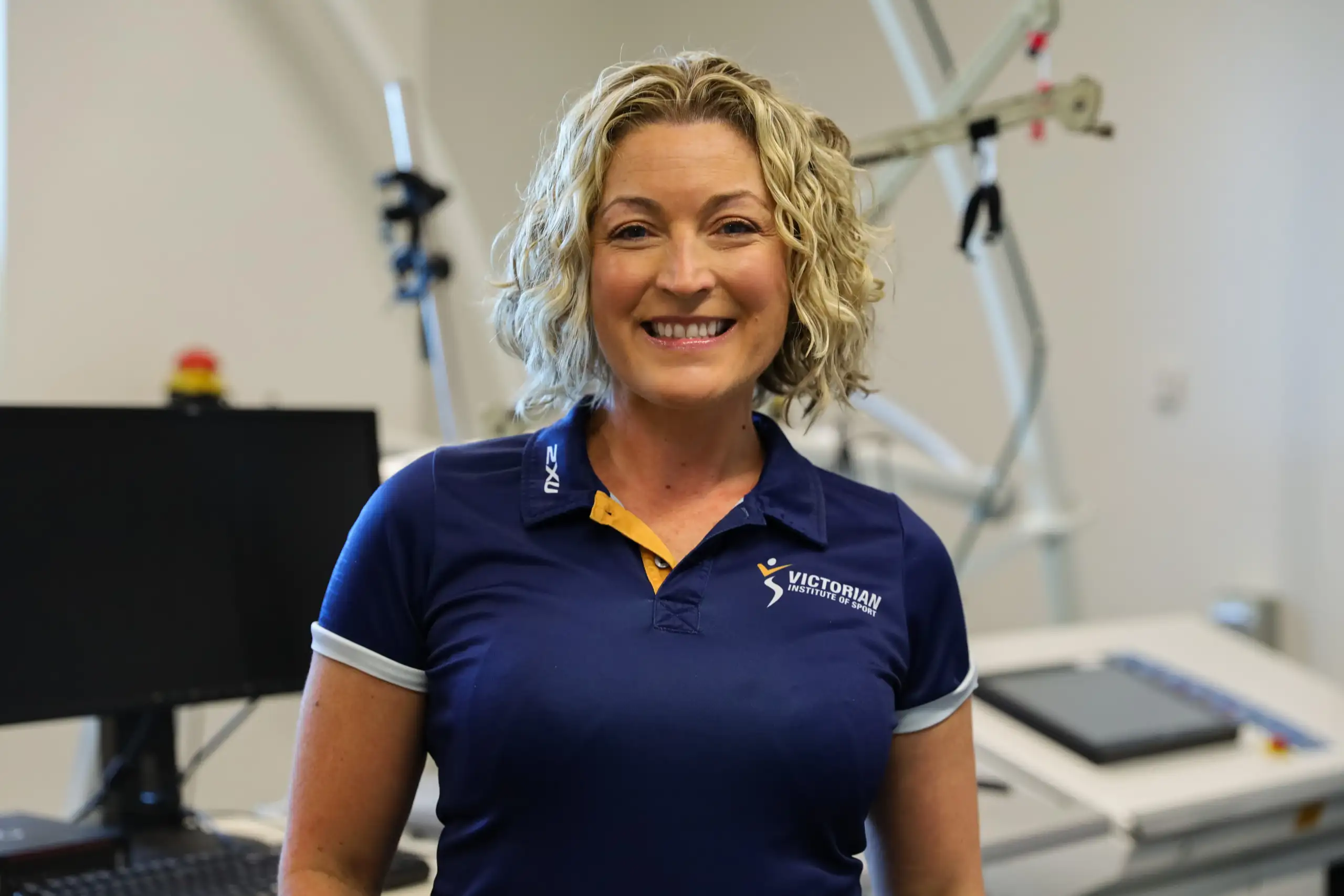 A photo of a lady with short curly blonde hair, smiling to camera wearing a blue VIS branded polo.