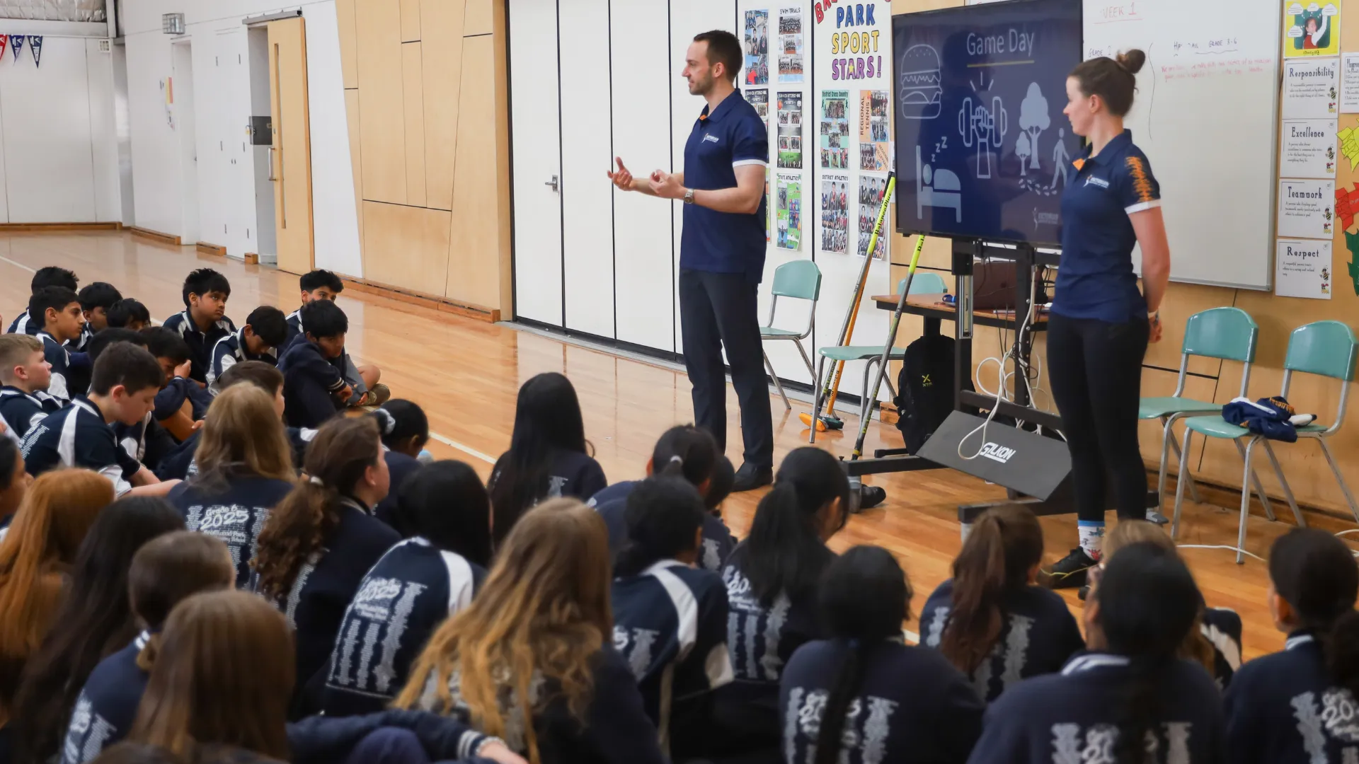 A male and female presenting to about 30 school students who are sitting in front of them.