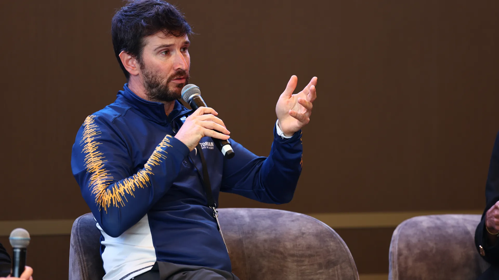 A photo of a male with short blonde hair in his twenties, public speaking to a room of adults.