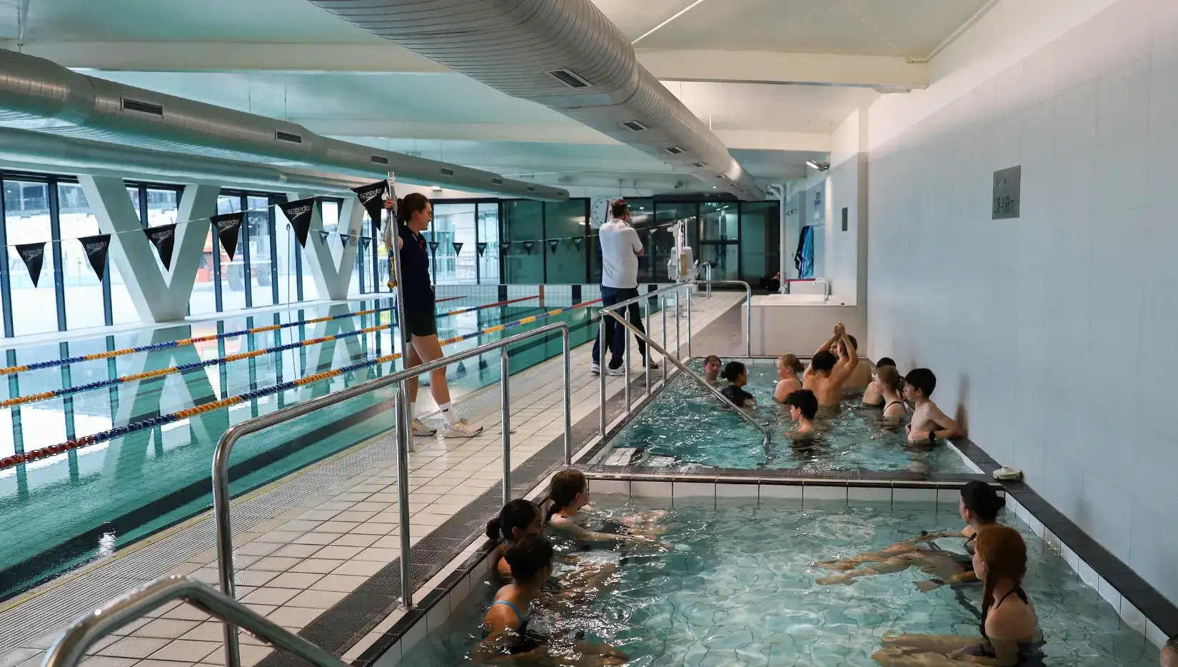 A photo of a male with short blonde hair in his twenties, public speaking to a room of adults.