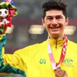 A male athlete in his thirties wearing a yellow Australian Paralypmic Team uniform, holding a bronze medal and a toy in his hand.