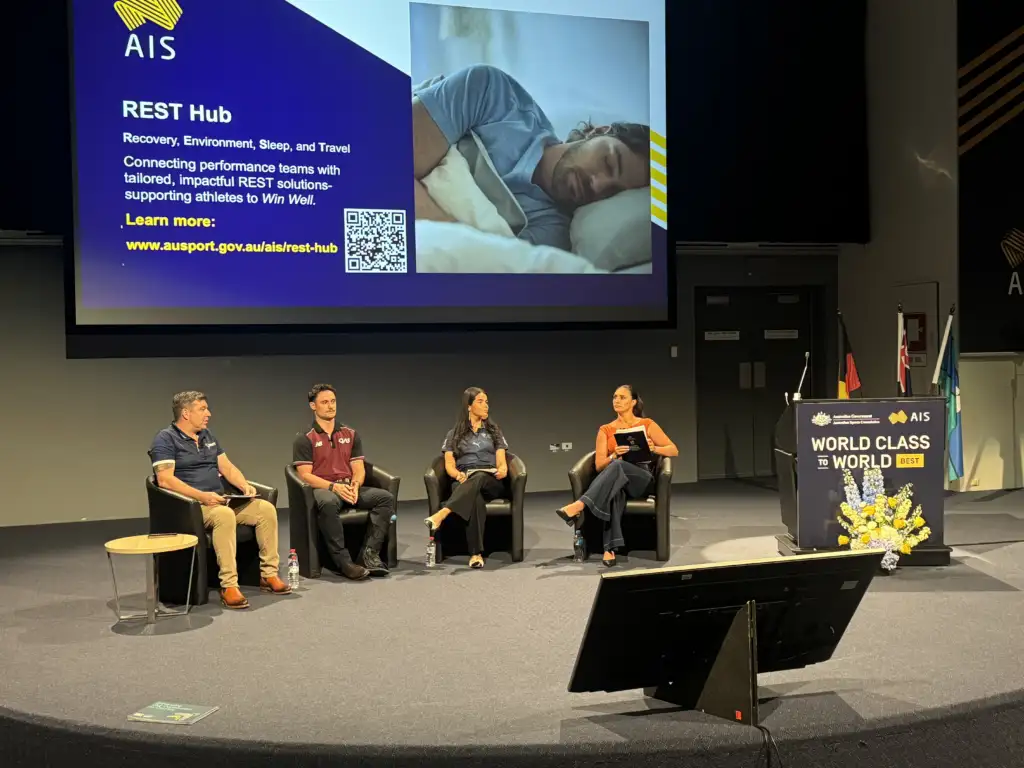 Four people sit on a large stage in a panel conversation with an AIS presentation in the background.