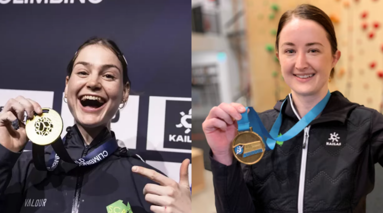 Two women hold gold medals up and are smiling celebrating their wins