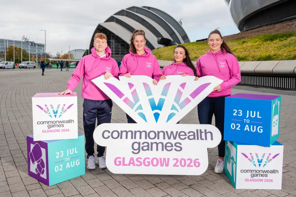 Four individuals in pink smiling for the camera in front of a sign.
