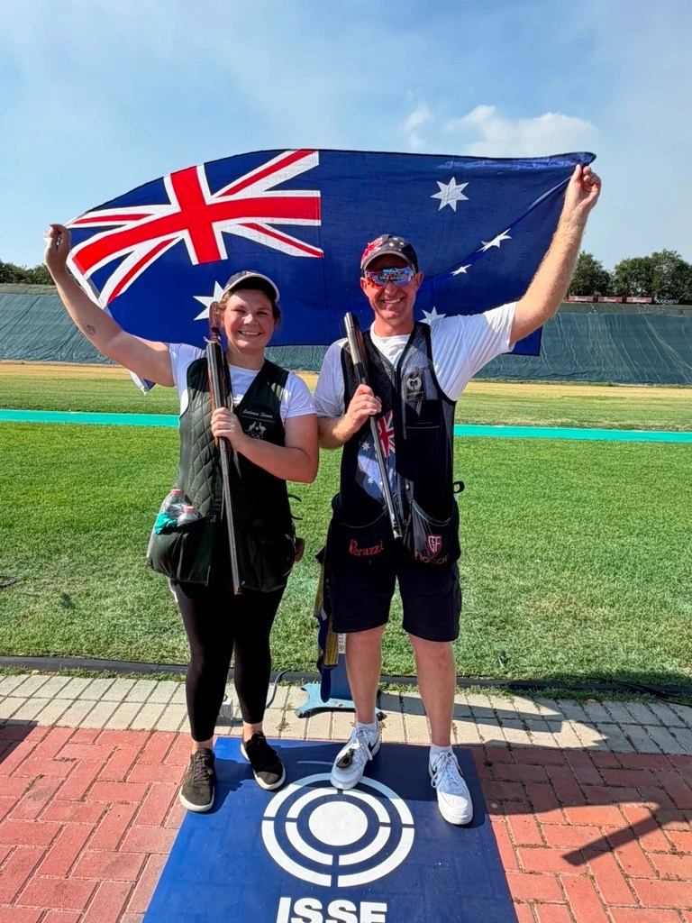 James Willett and Catherine Skinner celebrating by holding up Australian Flag and smiling at the ISSF Shotgun World Cip 2026.